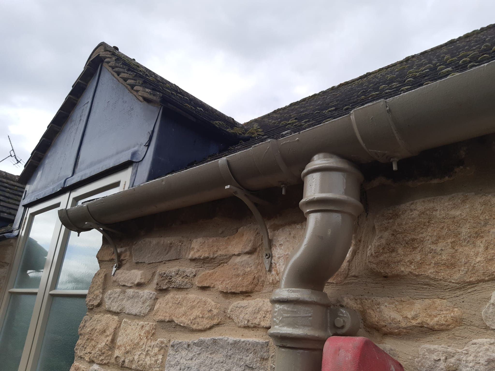 Cast iron guttering and downpipe installed on cotswold stone building near Burford with bespoke rise and fall brackets